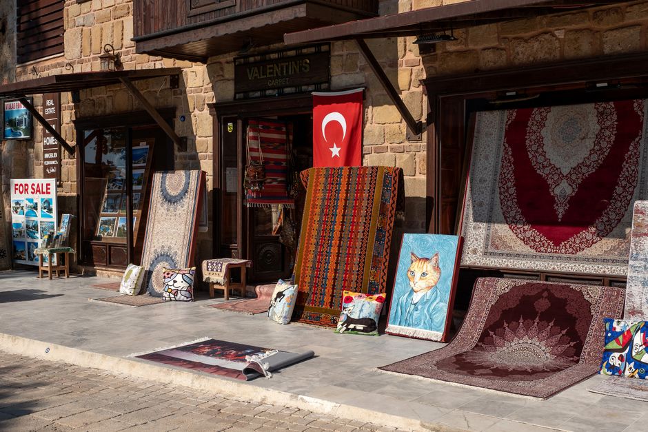 An outdoor display of various carpets and rugs arranged outside a shop on Ruislip High Street. The carpets, made of materials like wool and other textiles, feature intricate patterns and vibrant color